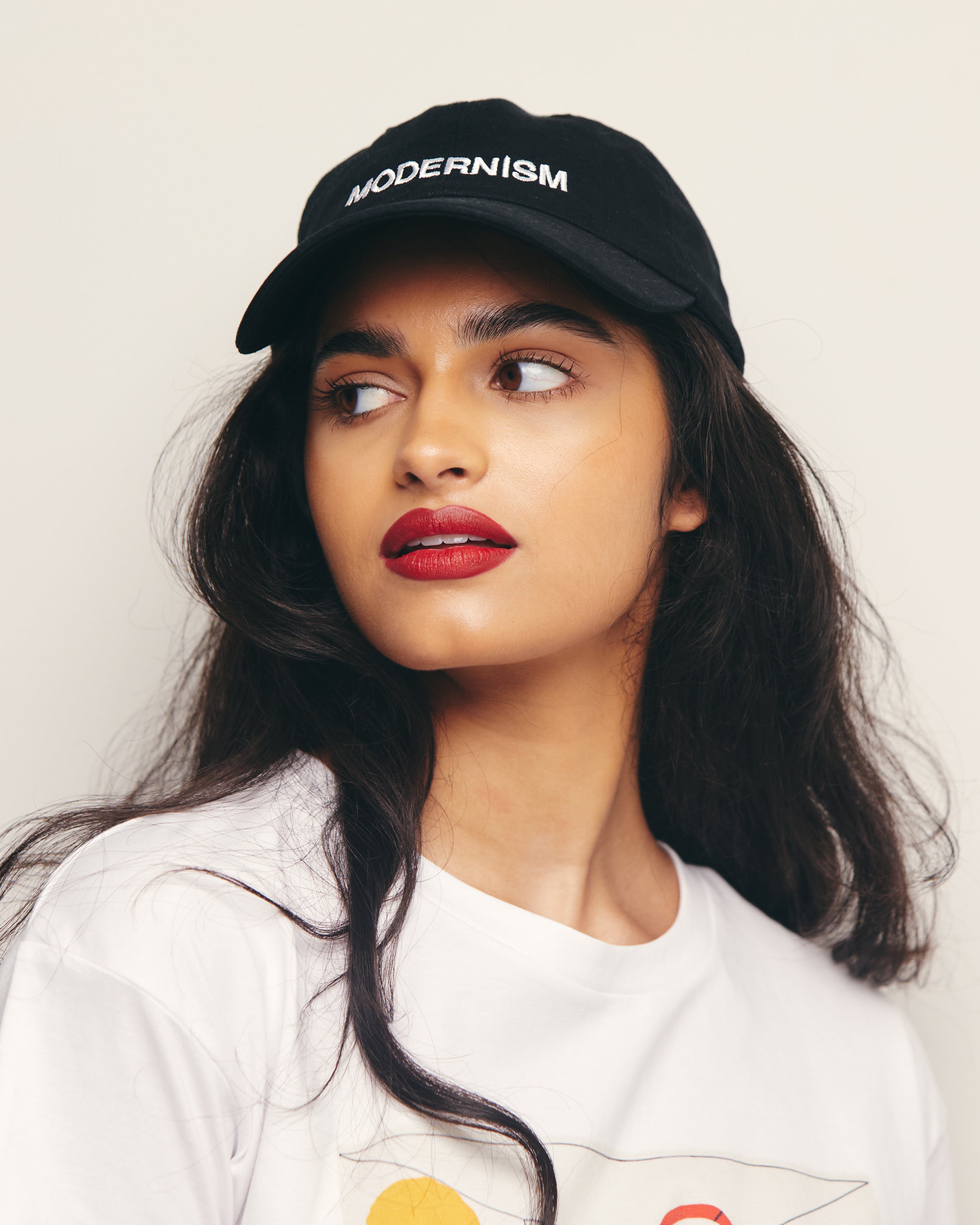 Mira Bhat wears Black Baseball Cap / Dad Hat with Modernism Art Movement Text Embroidery on Front. 100% Cotton.