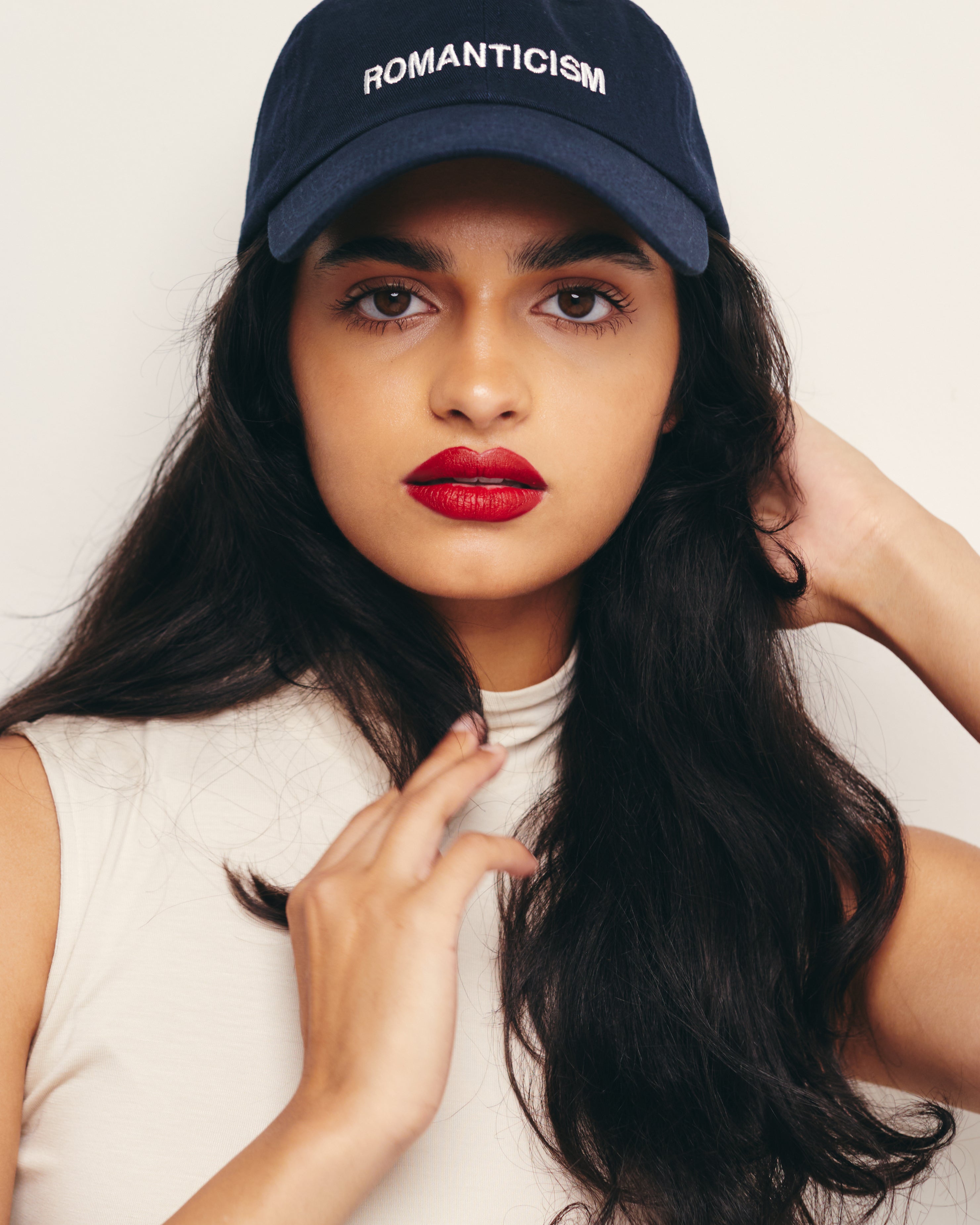 Mira Bhat wears Outsider Supply Navy Blue Dad Hat with Romanticism Art Movement Embroidery Text.