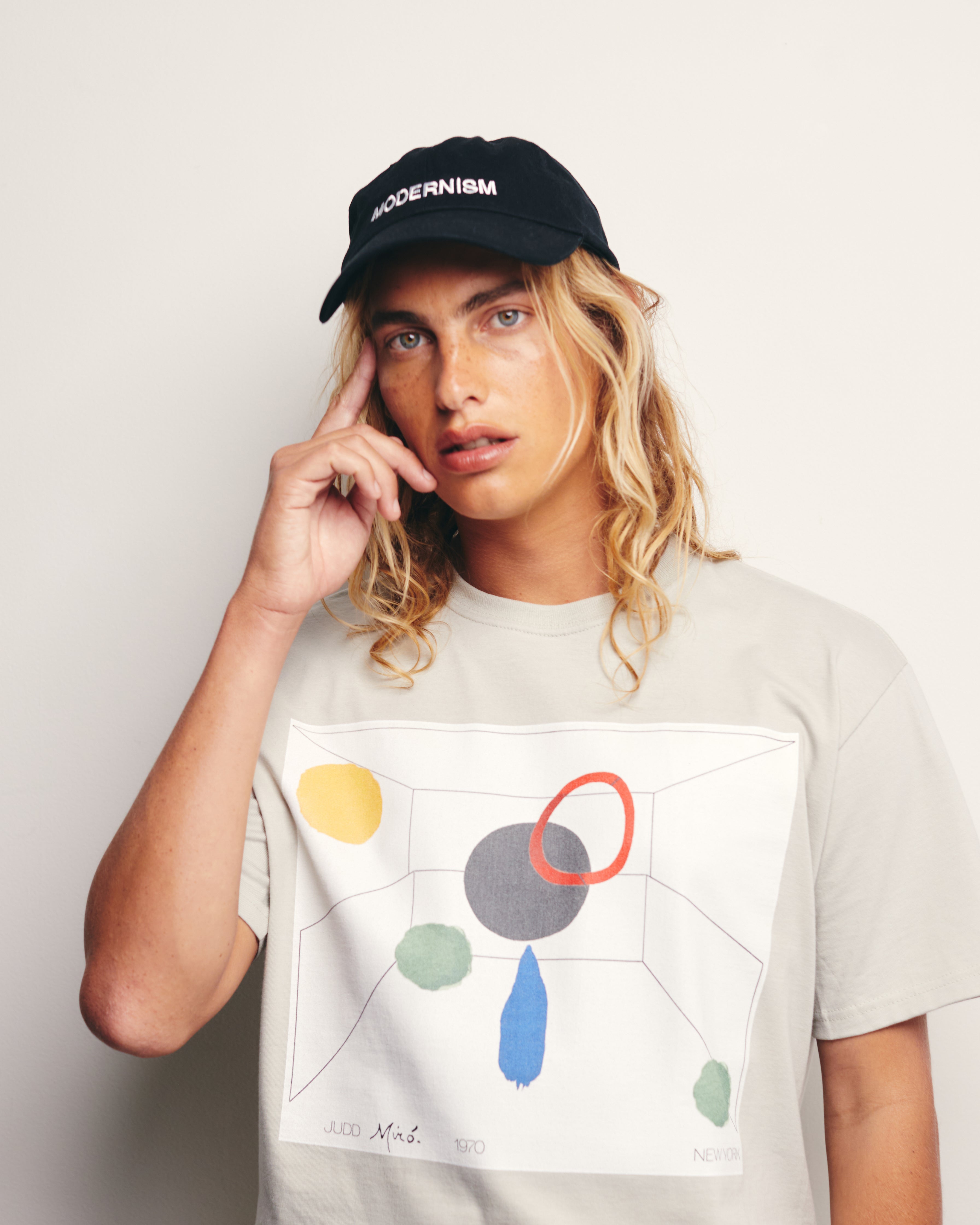 Lucas Ucedo wears Gray/ Putty Organic Short Sleeve 100% Cotton Tee with graphic print of an imaginary Exquisite Corspe collaboration between Donald Judd and Joan Miro.