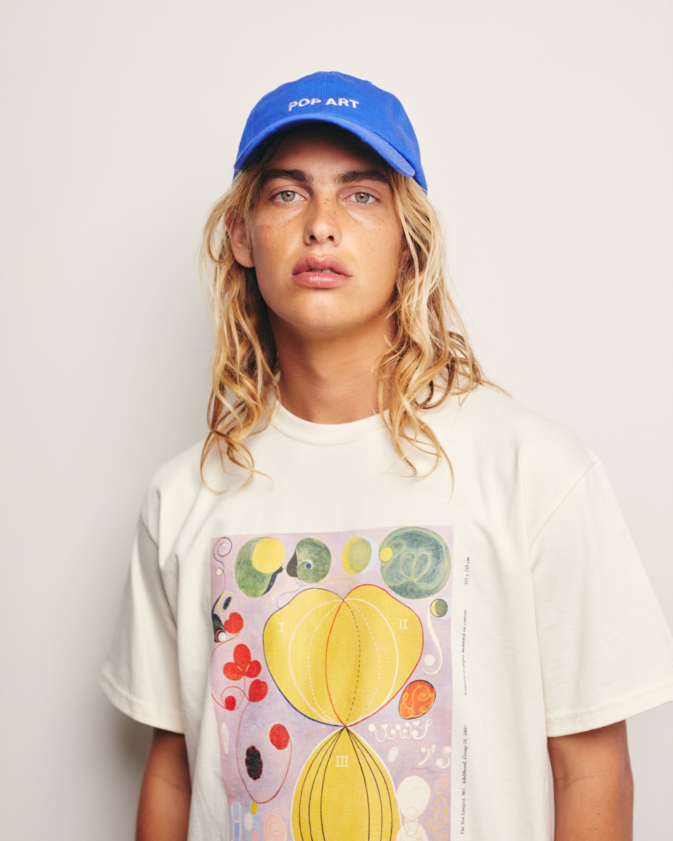 Lucas Ucedo Wears Royal Blue Dad Hat with White Pop Art Embroidery and 100% Organic Cotton Off White Tee with Hilma af Klint Abstract Expressionism Painting Graphic Print The Ten Largest