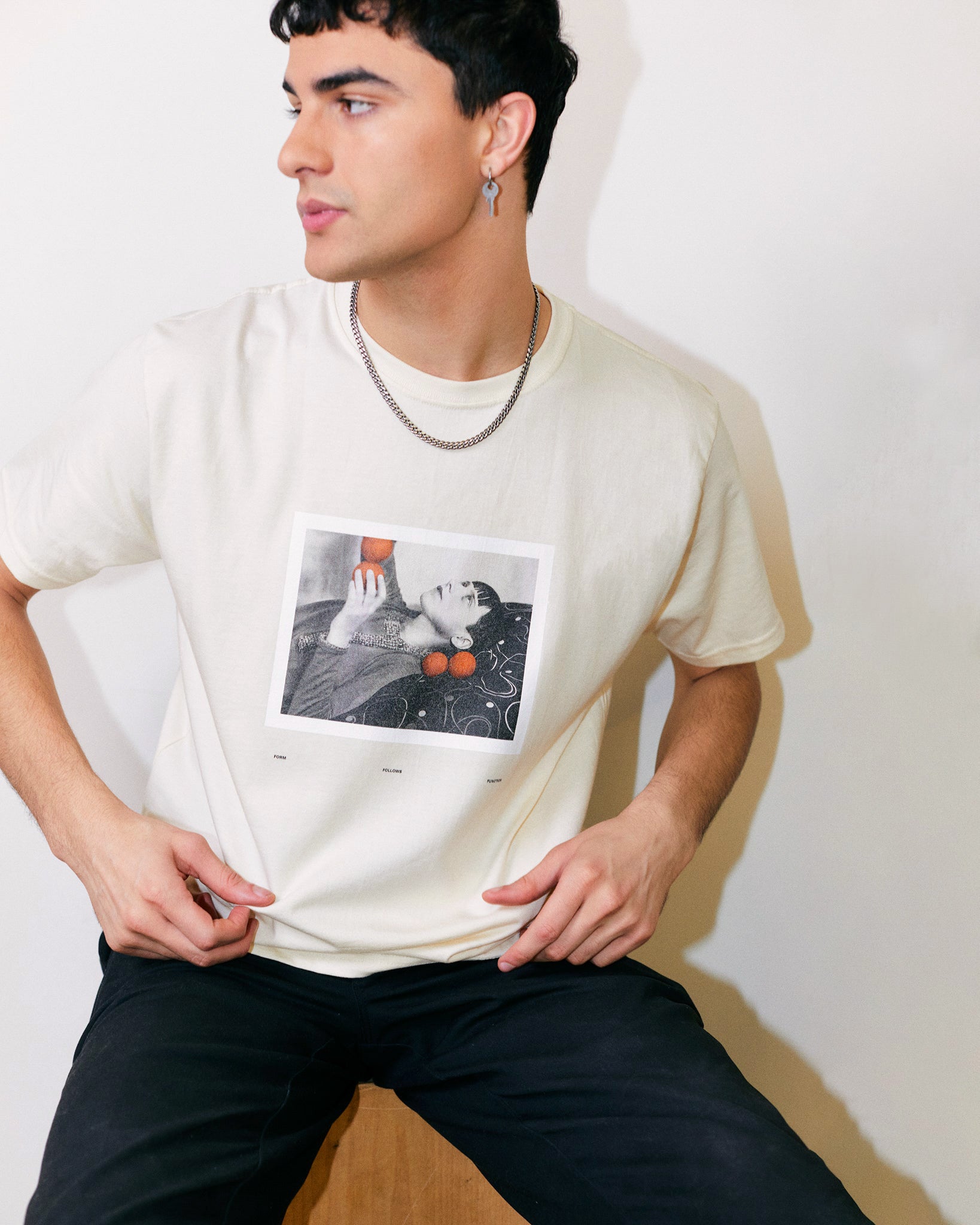 Arjang Mahdavi wears Cream/ Off White/ Ceramic Organic Short Sleeve 100% Cotton Tee with a print of Bauhaus Student Margaret Leiteritz and Form Follows Function Orange Graphic Text on the back from the Bauhaus Collection. 
