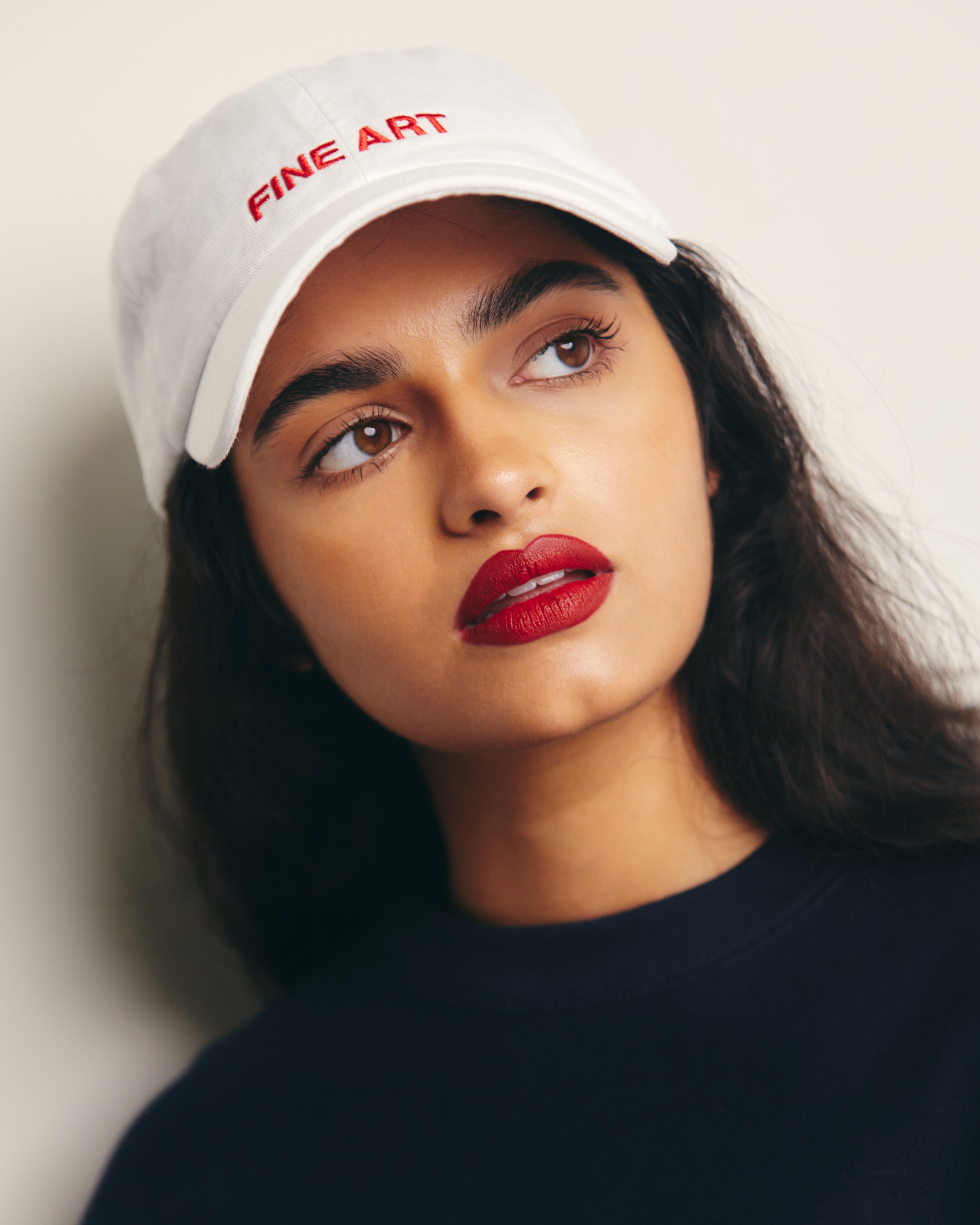 Mira Bhat wears White Baseball Cap / Dad Hat with Fine Art Movement Red Text Embroidery on Front. 100% Cotton.