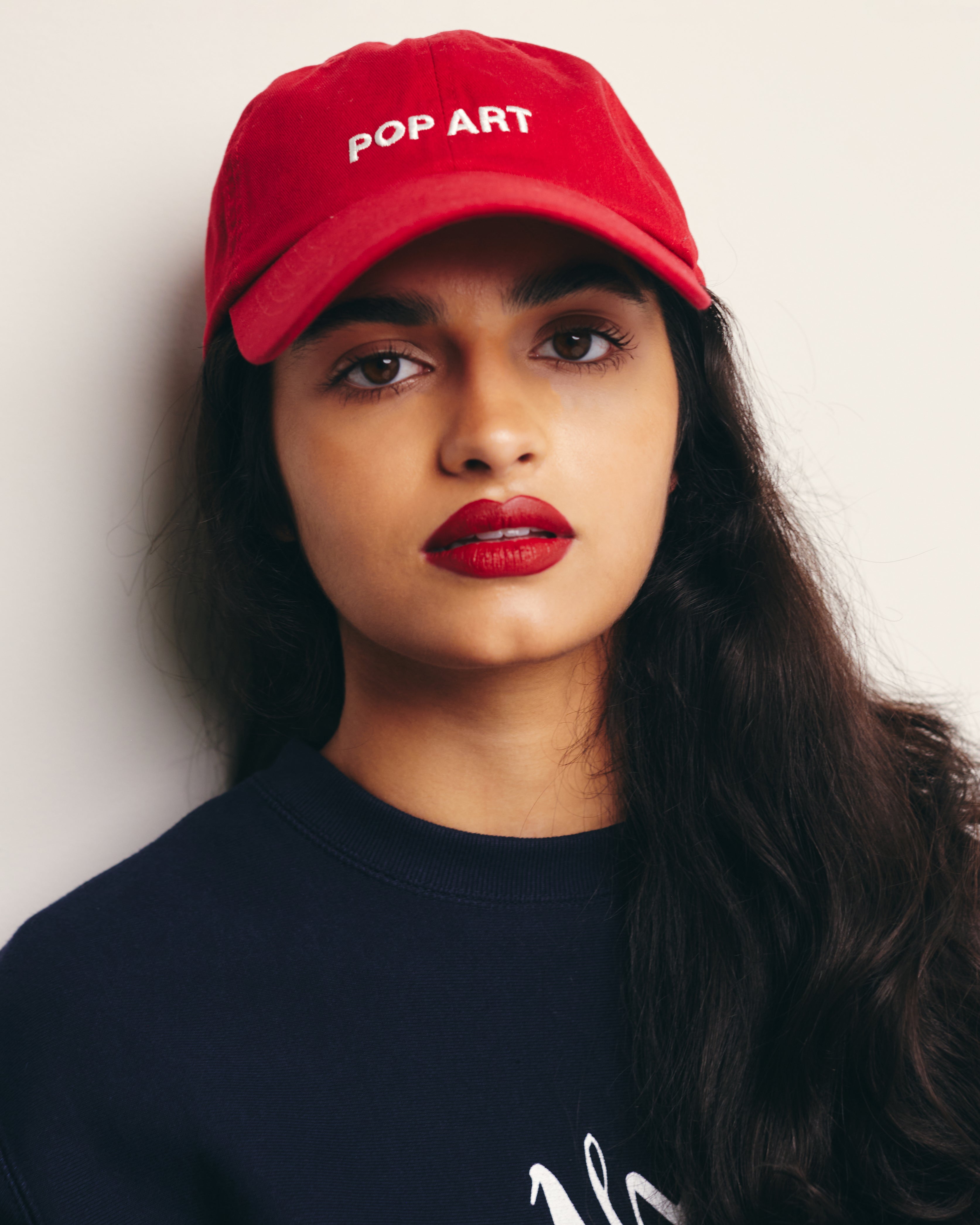 Mira Bhat wears Red  Baseball Cap / Dad Hat with Pop Art Movement Text Embroidery on Front. 100% Cotton.