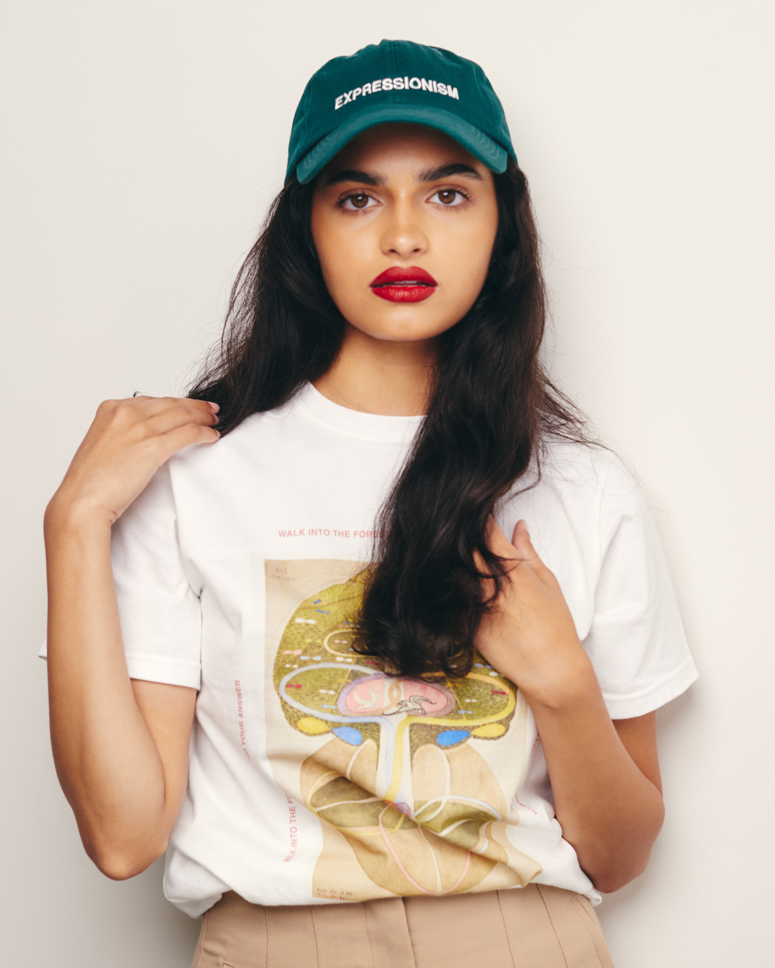 Mira Bhat Wears 100% Cotton Green Baseball Cap / Dad Hat with Expressionism Art Movement Text Embroidery on Front with 100% Organic Cotton White Tshirt / Tee / T-shirt with Hilma af Klint Tree of Knowledge Graphic Print.