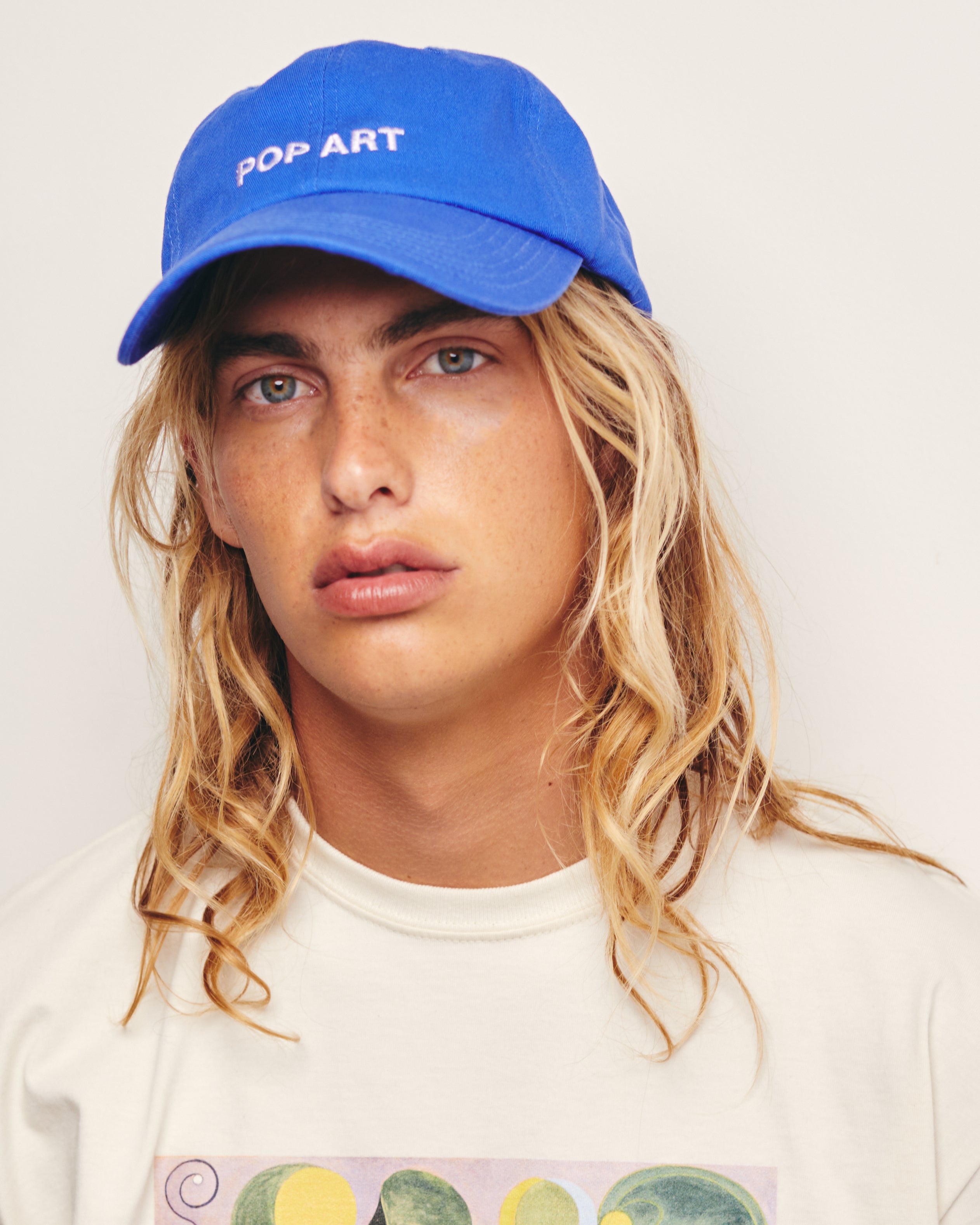 Lucas Ucedo wears Blue  Baseball Cap / Dad Hat with Pop Art Movement Text Embroidery on Front. 100% Cotton.