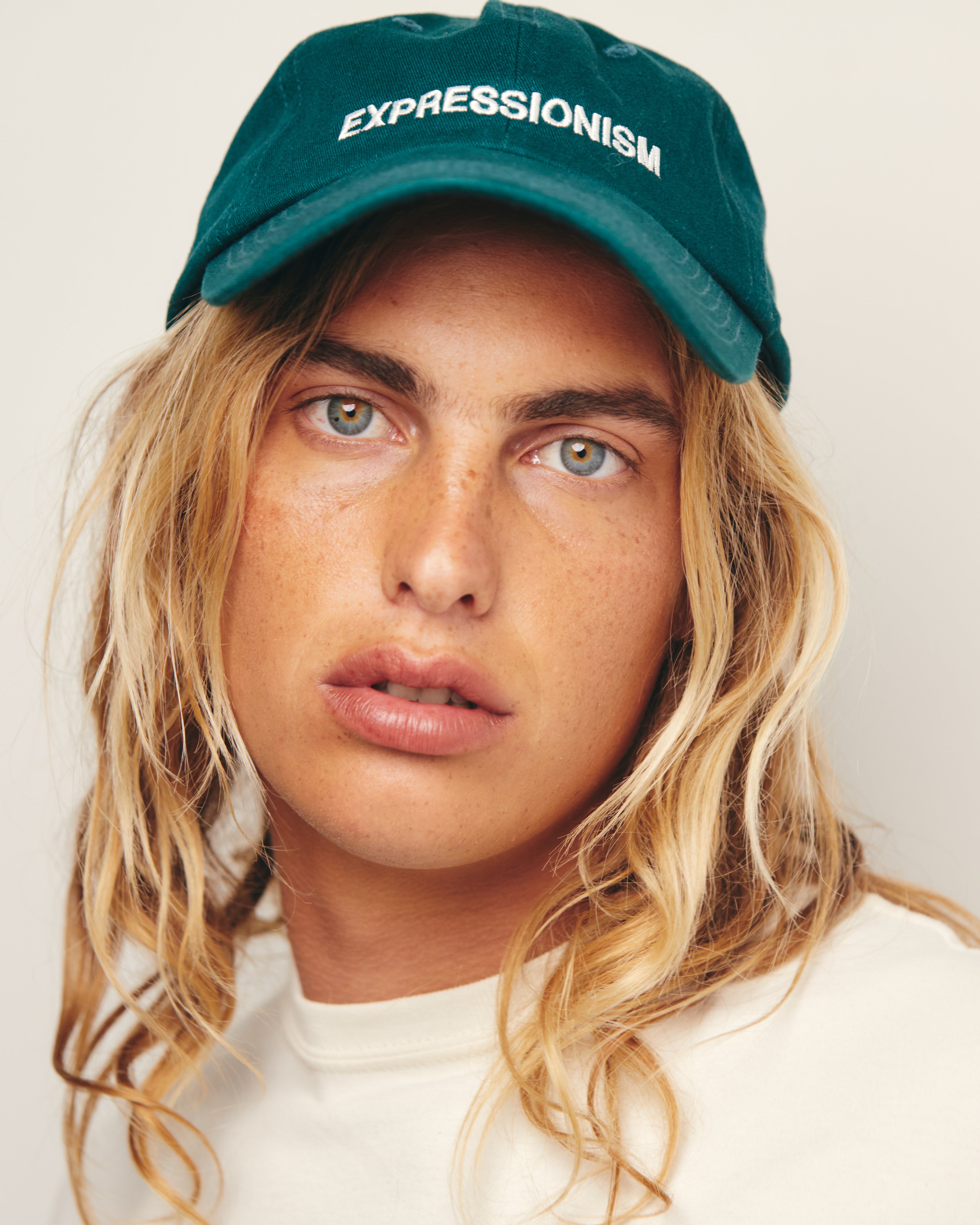 Lucas Ucedo wears Green Baseball Cap / Dad Hat with Expressionism Art Movement Text Embroidery on Front. 100% Cotton.