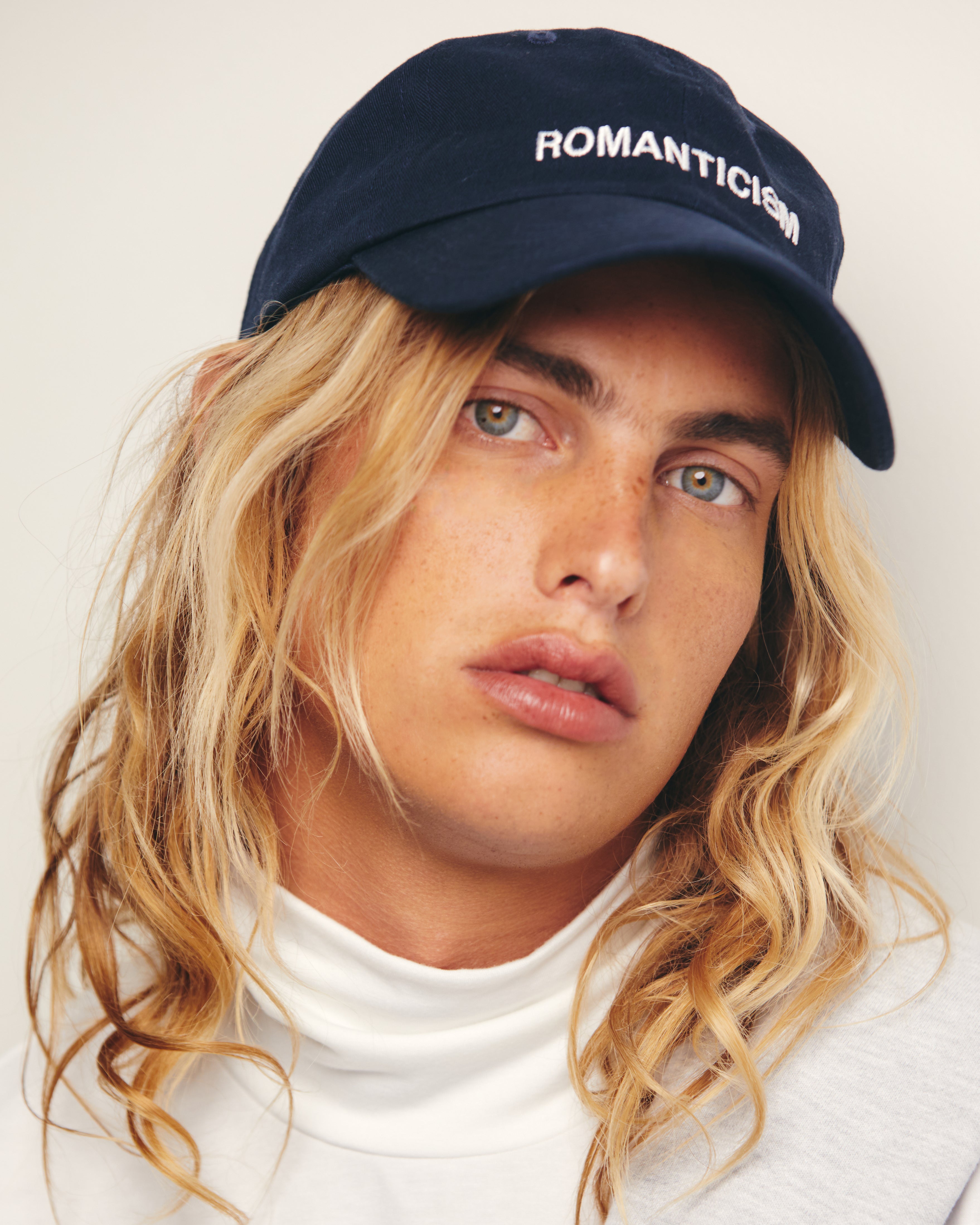 Lucas Ucedo wears Outsider Supply Navy Blue Dad Hat with White Romanticism Art Movement Embroidery Text.