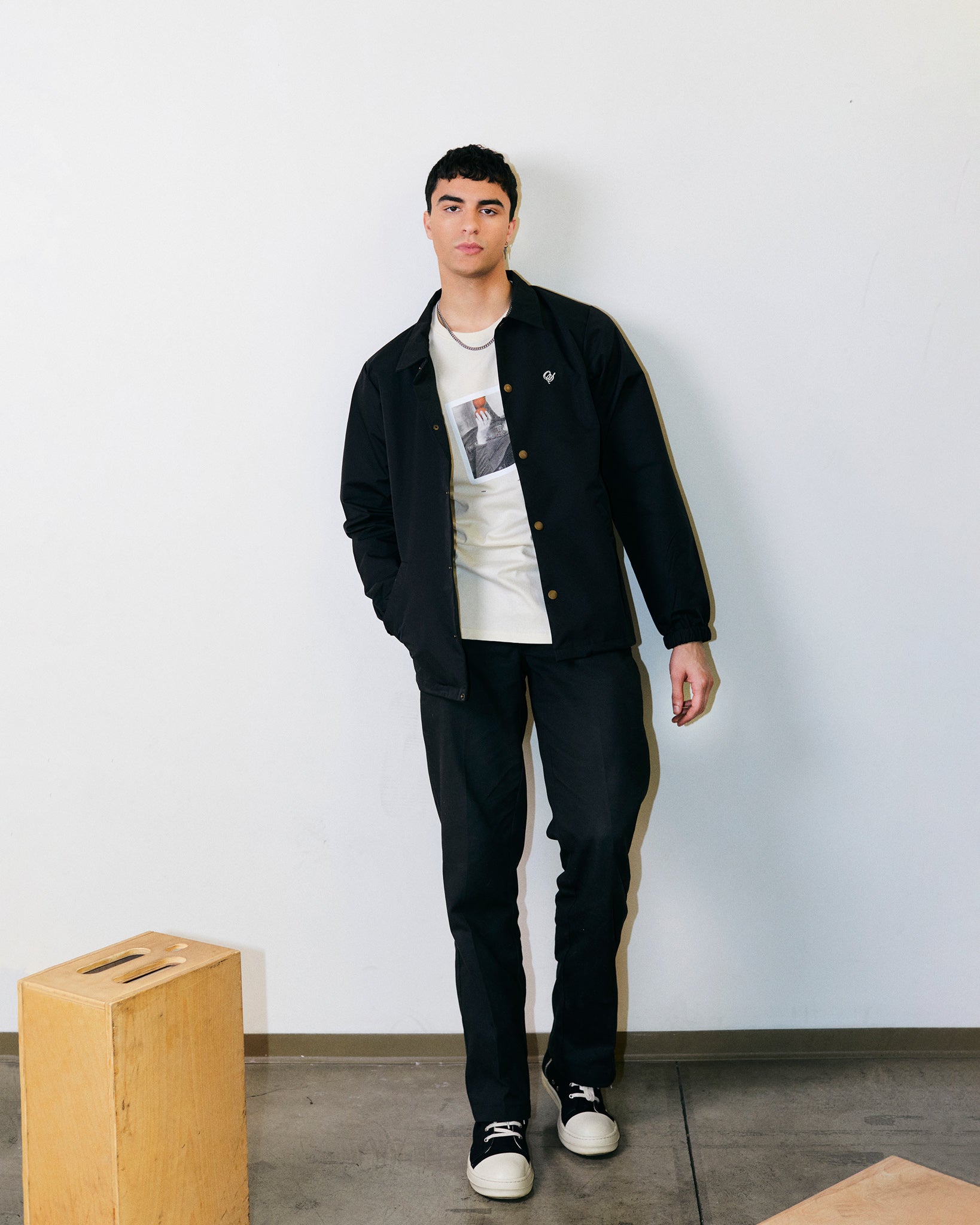 Arjang Mahdavi wears Black Mid-Weight Artist Smock Jacket with embroidered Outsider Supply Script. 100% Nylon. 