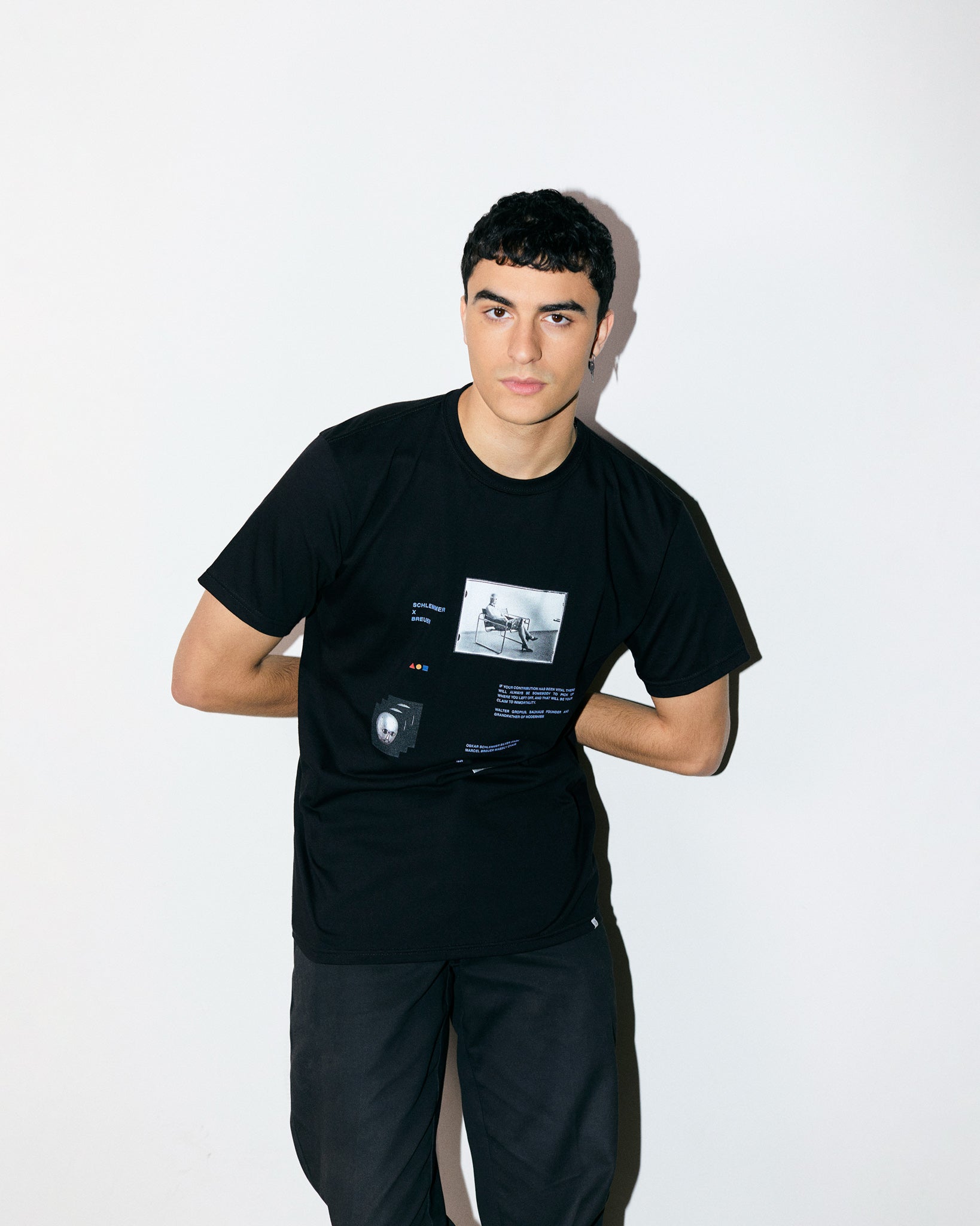 Arjang Mahdavi wears Black  Organic Short Sleeve 100% Cotton Tee with graphic print of Marcel Breuer’s B3 Chair and theatrical mask by Oskar Schlemmer and quote from Walter Gropius from the Bauhaus Collection. 